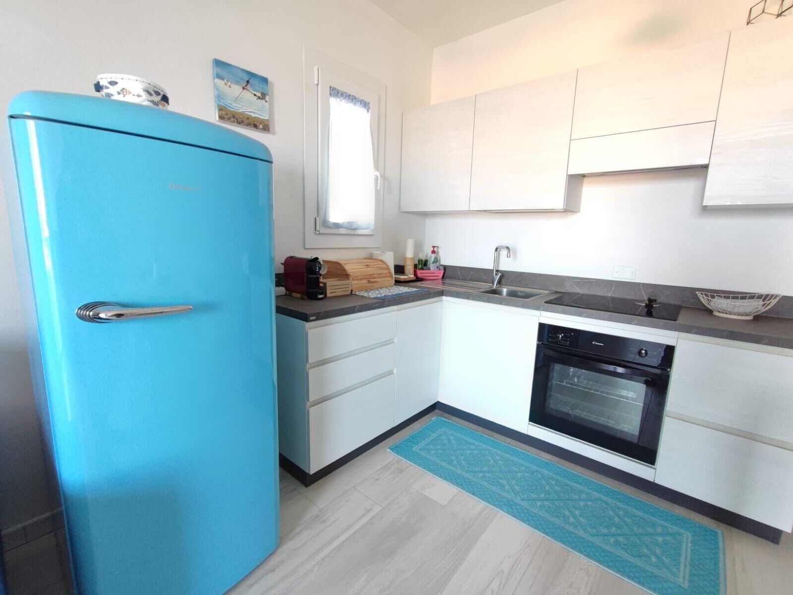 Eine kompakte Küche mit blauem Kühlschrank, weißen Schränken, einem schwarzen Ofen und einem Spülbecken.