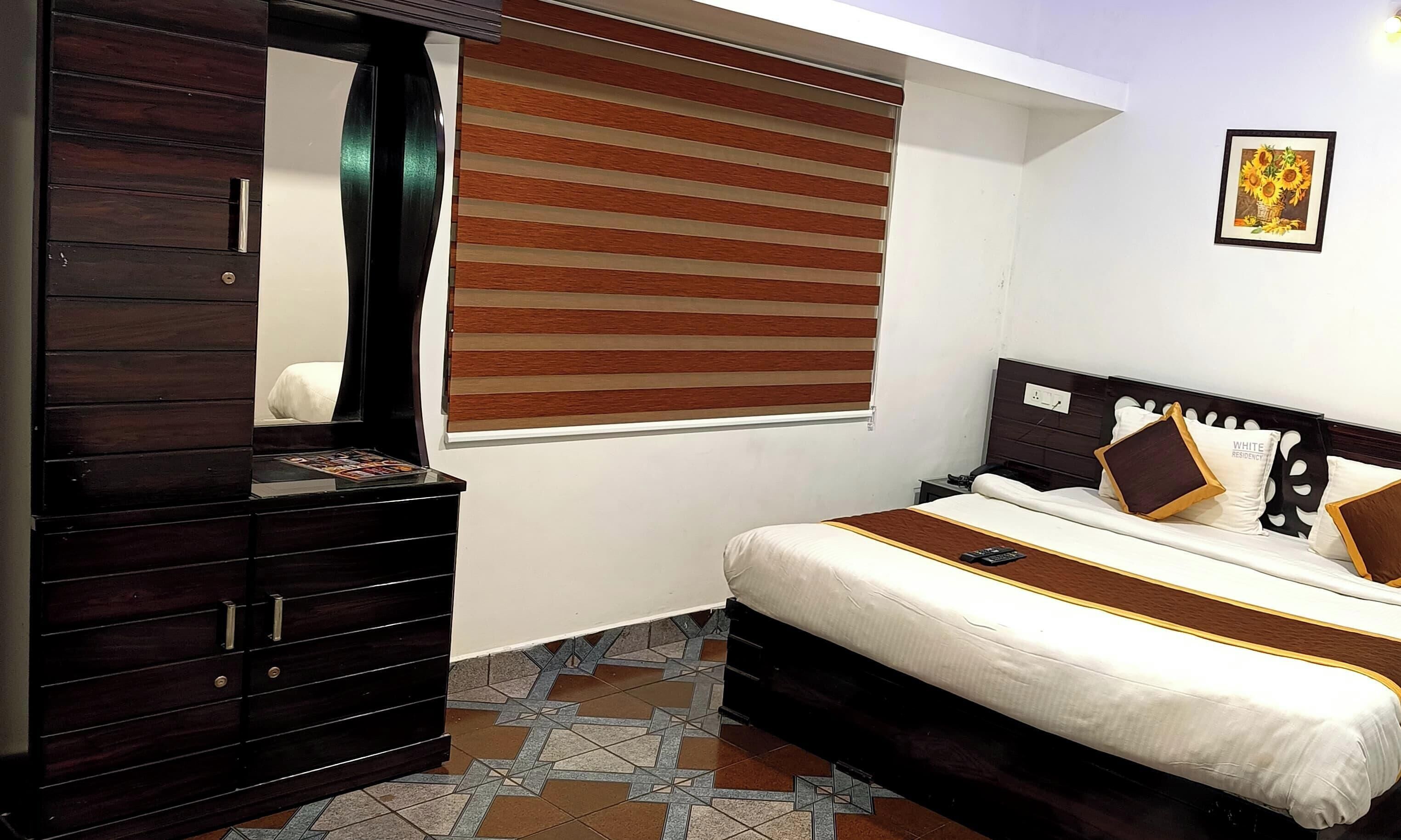 A bedroom with a bed, a dresser, a window with blinds, and a framed picture on the wall.
