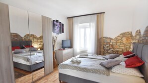 A bedroom with a bed, a TV, a mirror, and a stone wall. - Cozy Apartment With Garden (Umag)