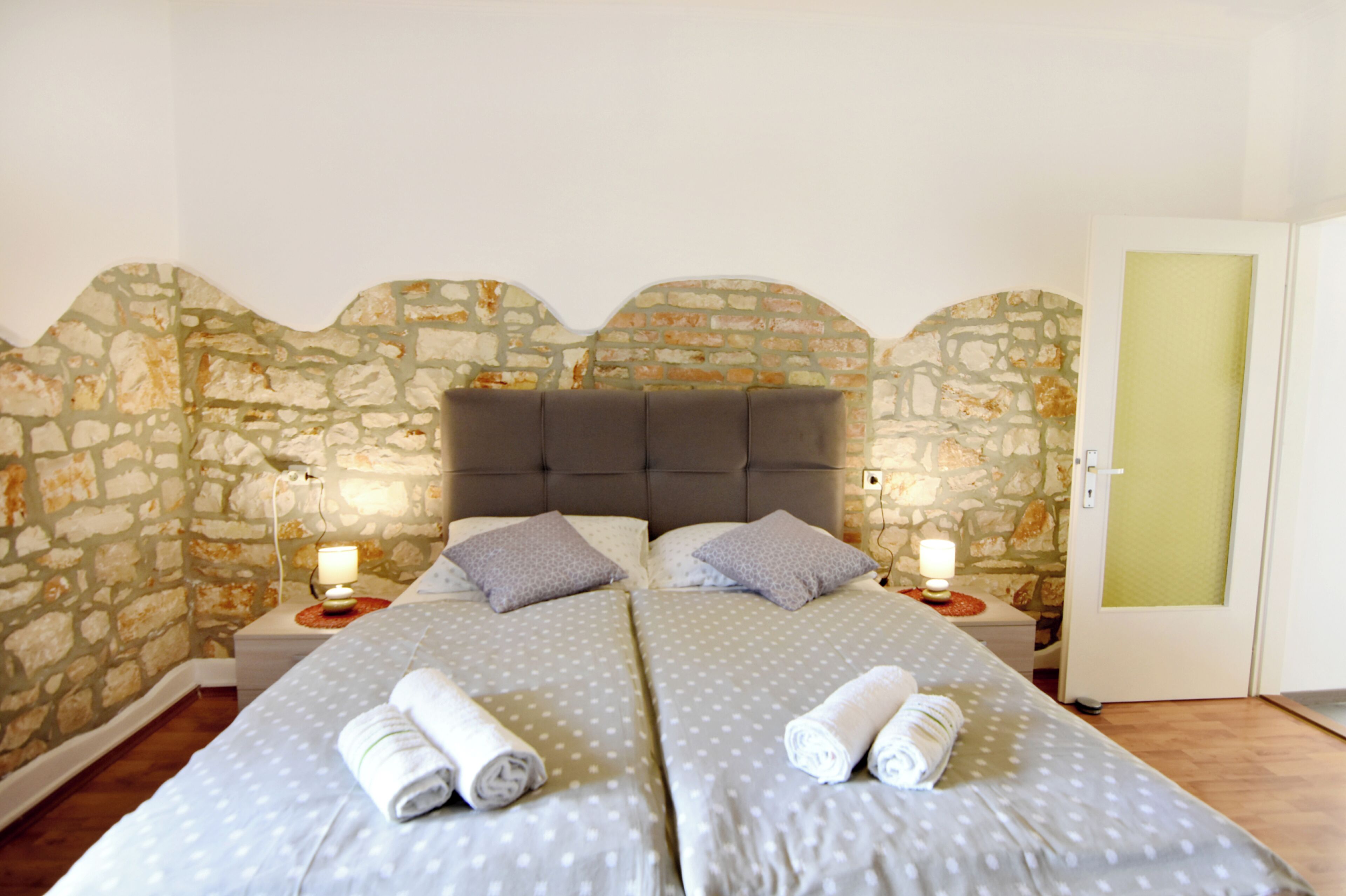 Una cama doble con dos almohadas, pared de piedra, suelo de madera y una puerta con panel verde.