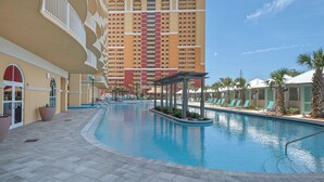 A swimming pool with lounge chairs, a covered seating area, and a high-rise hotel in the background.