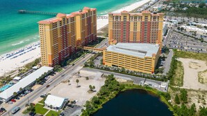 A high-rise hotel with multiple floors, a parking lot, and a beach view.