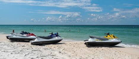 A beach with three jet skis parked on the sand, a clear sky, and the ocean in the background.