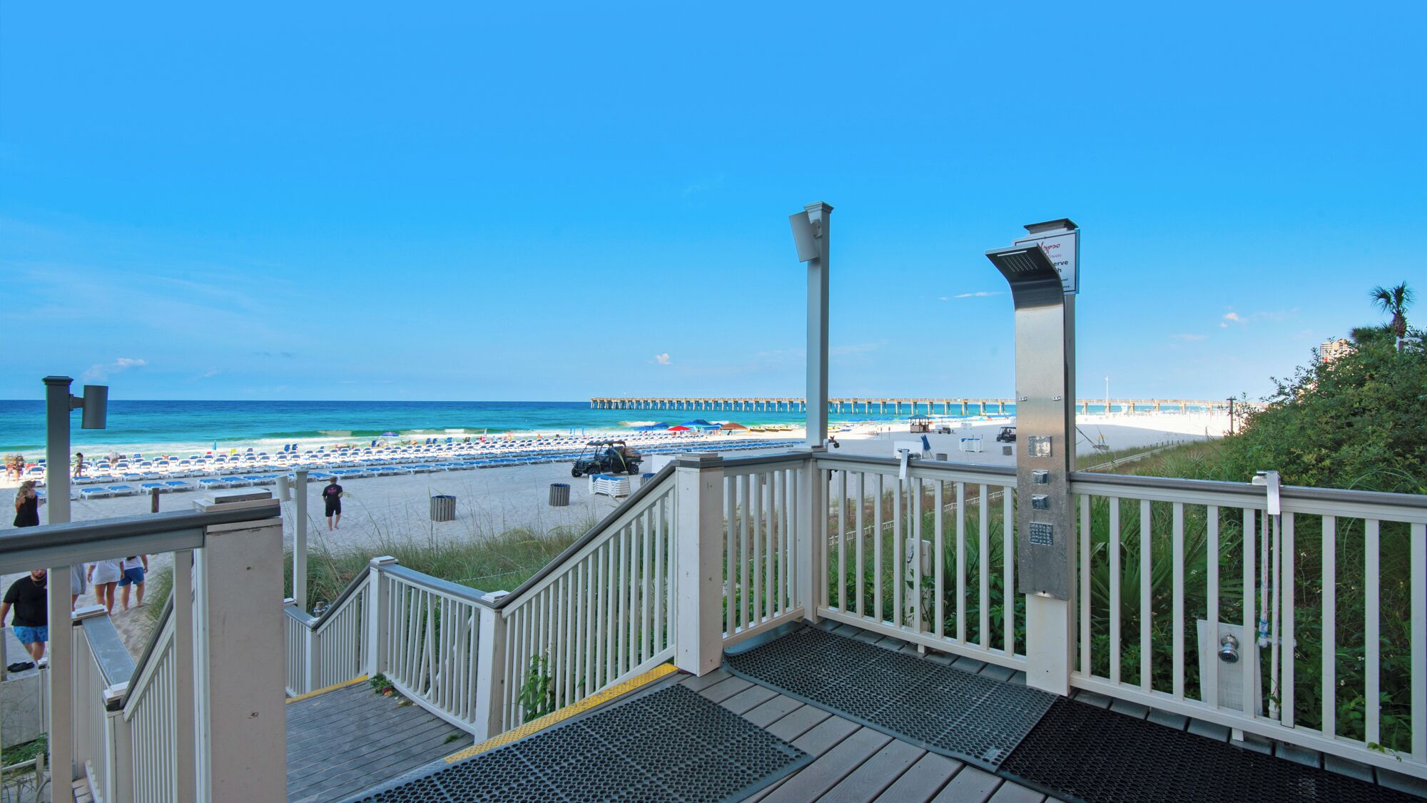 Une vue sur la plage depuis un balcon doté d’une balustrade, une jetée au loin et des parasols sur la plage.