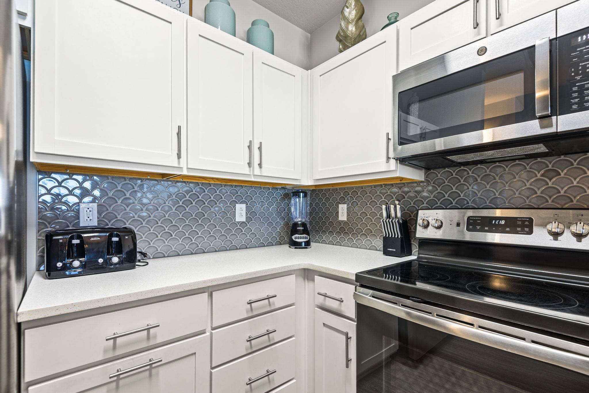 A kitchen with white cabinets, a microwave, an oven, a toaster, and a blender.