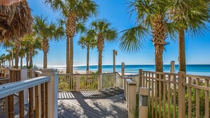 A wooden deck leading to a beach with palm trees and a clear blue sky.