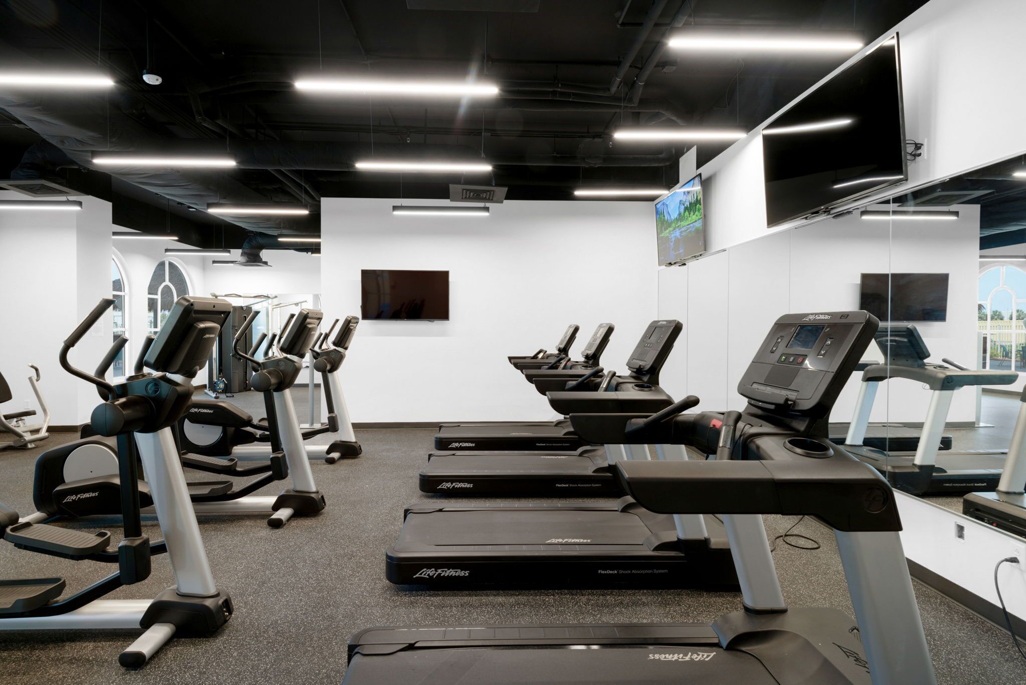 A gym with treadmills, ellipticals, and a TV screen.