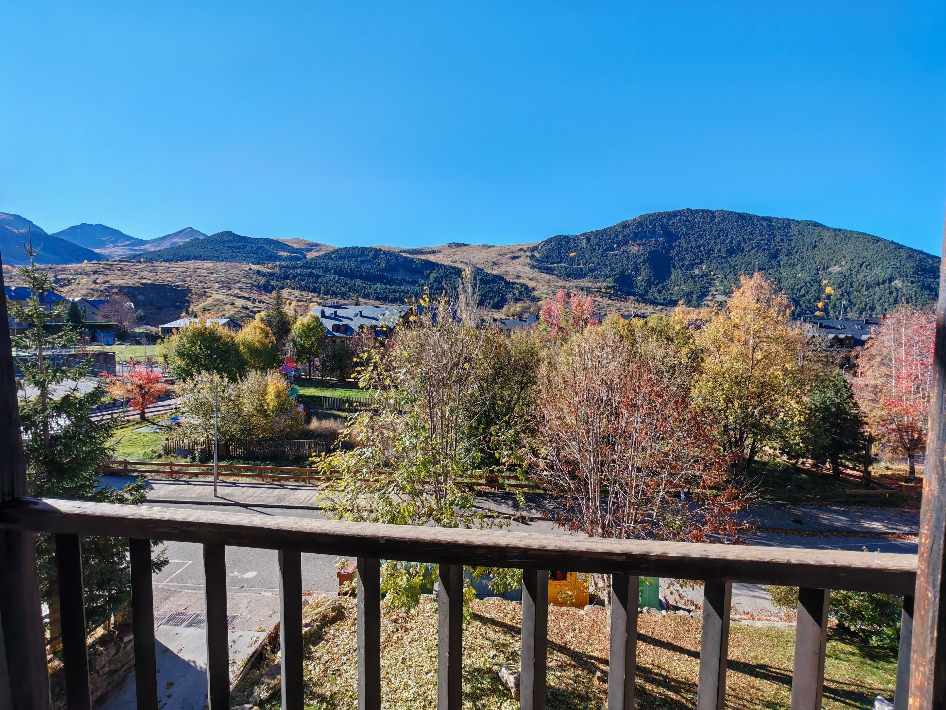A view from a balcony overlooking a residential area with houses, trees, and mountains in the background.