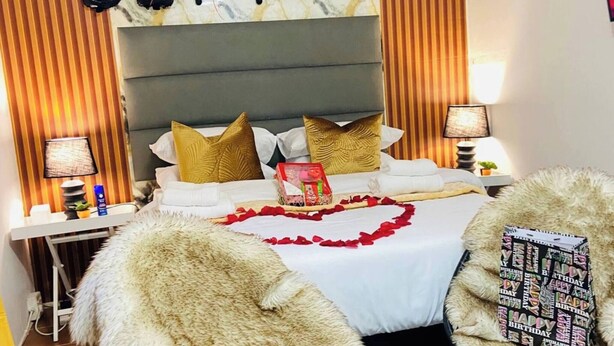 A bedroom with a bed, pillows, a bedside table, a nightstand, a wall with a birthday decoration, and a fluffy rug. - Room-cosy & Private Cottage With Easy ac (Pietermaritzburg)