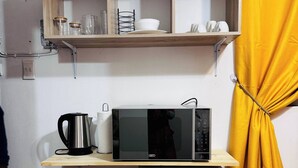 A compact kitchenette with a microwave, a small fridge, a shelf with kitchenware, and a yellow curtain. - Room-cosy & Private Cottage With Easy ac (Pietermaritzburg)