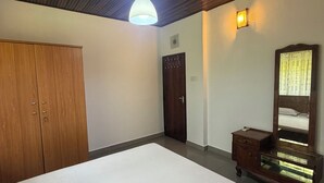 A bedroom with a wooden ceiling, a bed with white bedding, a wardrobe, a dresser with a mirror, and a wall-mounted light fixture.
