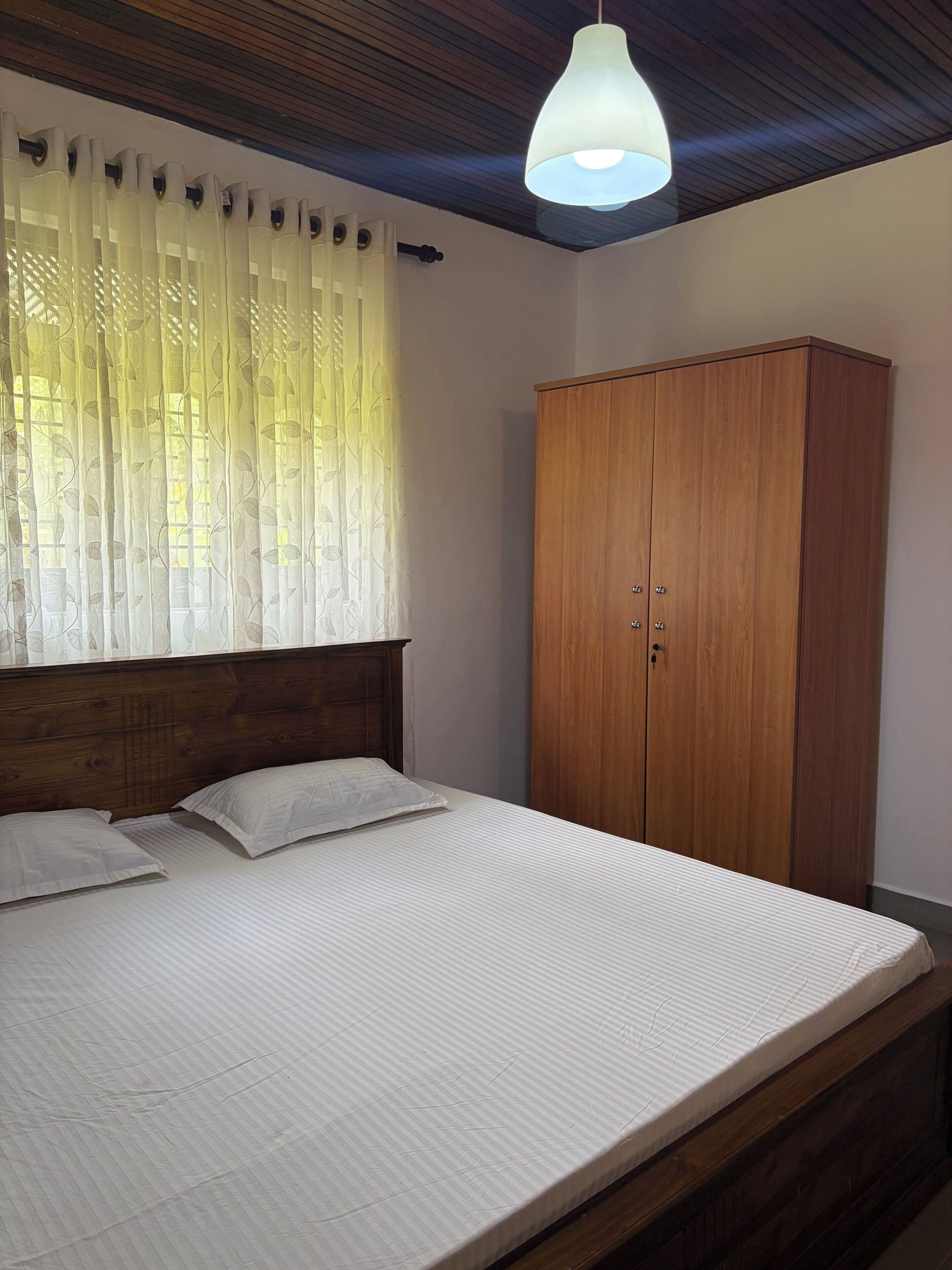 A bedroom with a bed, wooden wardrobe, and a hanging light fixture.