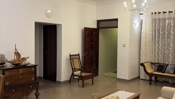 A living room with a sofa, a wooden coffee table, a chair, a dresser, and a door leading to another room.