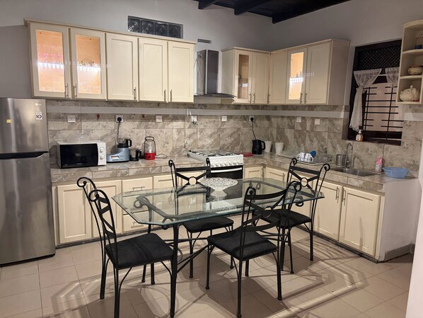 A modern kitchen with a glass dining table, four chairs, a refrigerator, a microwave, a stove, and cabinets.