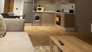 Een kleine keuken met moderne apparatuur, een eethoek met tafel en stoelen, en een bank.