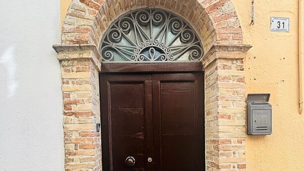 Puerta doble de madera con un arco metálico decorativo encima, incrustada en un muro de ladrillo de color amarillo.
