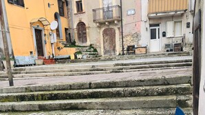 Un patio empedrado con escalones que conducen a un edificio de fachada amarilla y con un balcón.