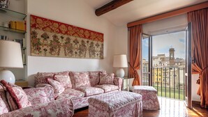 Un salon avec un canapé, un pouf et une grande fenêtre avec des rideaux.