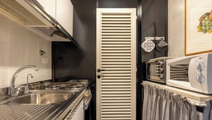 Une cuisine compacte dotée d’un évier en acier inoxydable, d’un four à micro-ondes et d’une porte à persiennes.