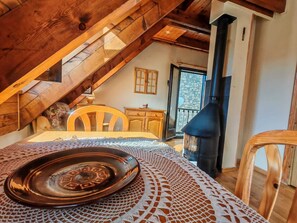 Ein gemütliches Dachzimmer mit einem Holztisch, einer gewebten Tischläufer, einem Kamin und Blick durch eine Glastür nach draußen.