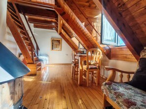 Ein Holzinnenraum mit schrägverdeckter Decke, einem Bett, einem Stuhl und einem Tisch.
