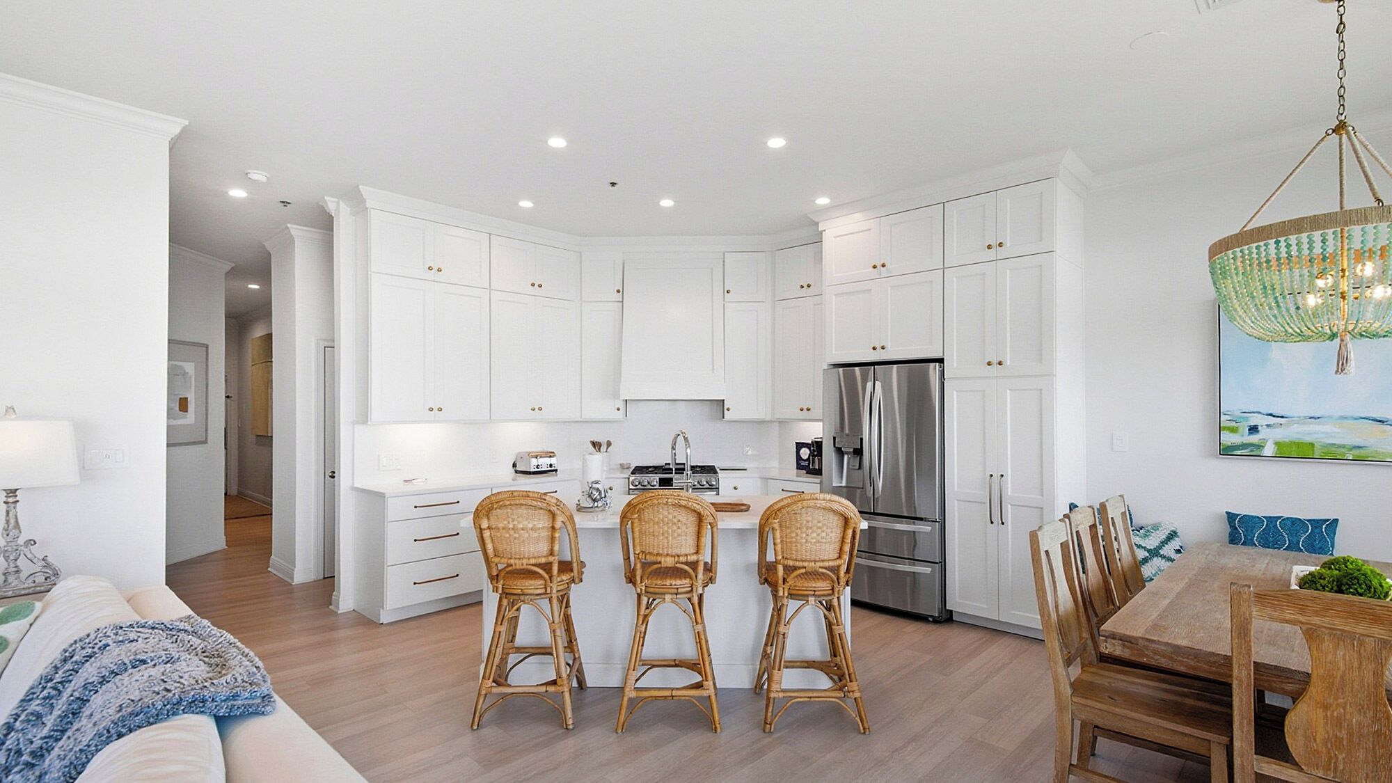 A modern kitchen with white cabinets, a stainless steel refrigerator, and a dining area with wicker chairs and a wooden table.