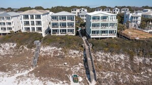 Ein Küstenhotel mit mehreren Gebäuden, einem Sandstrand und einer Holzpromenade, die zum Strand führt.