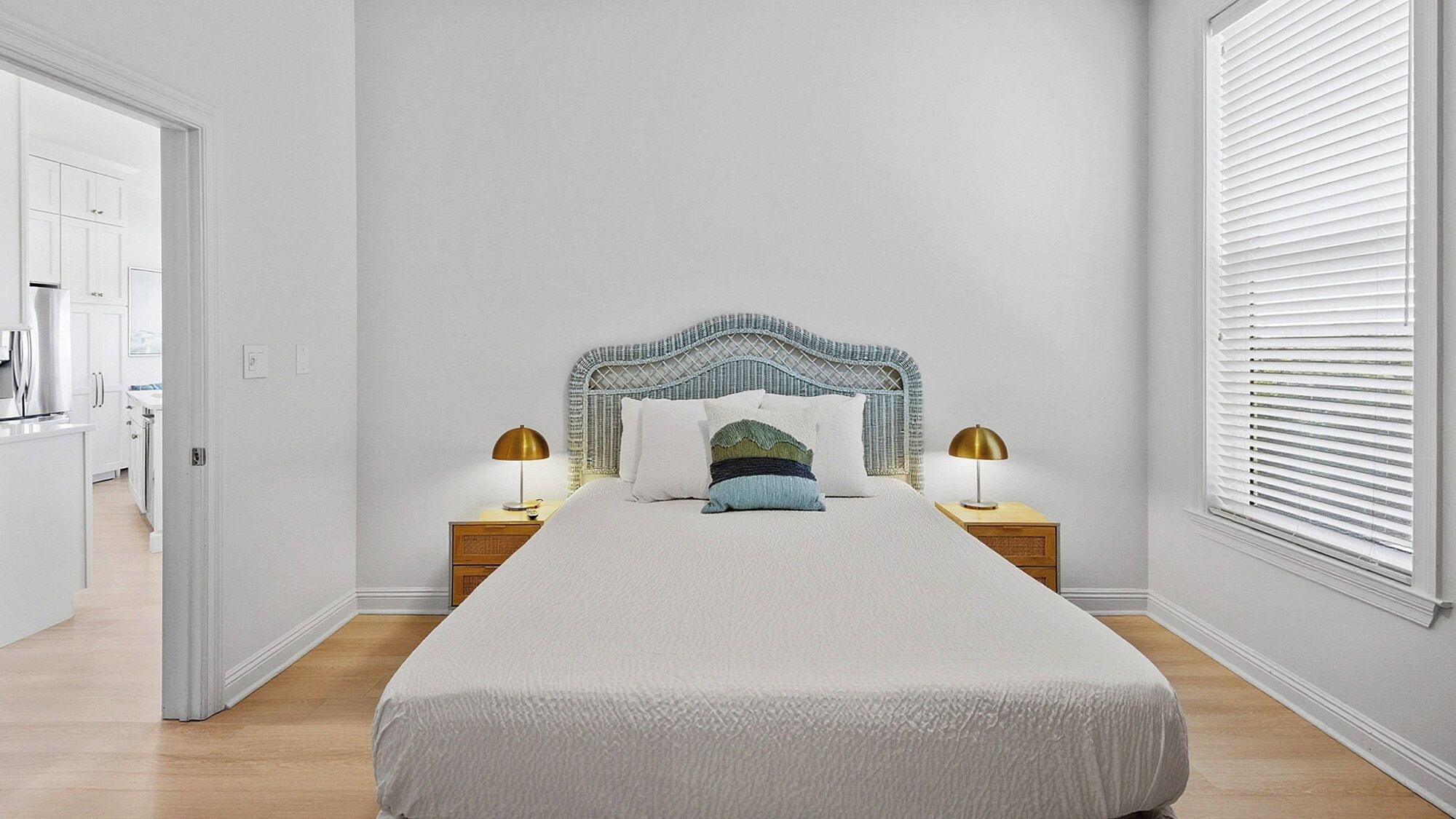 A bedroom with a large bed, a headboard with a decorative pattern, two bedside tables with lamps, and a window with blinds.