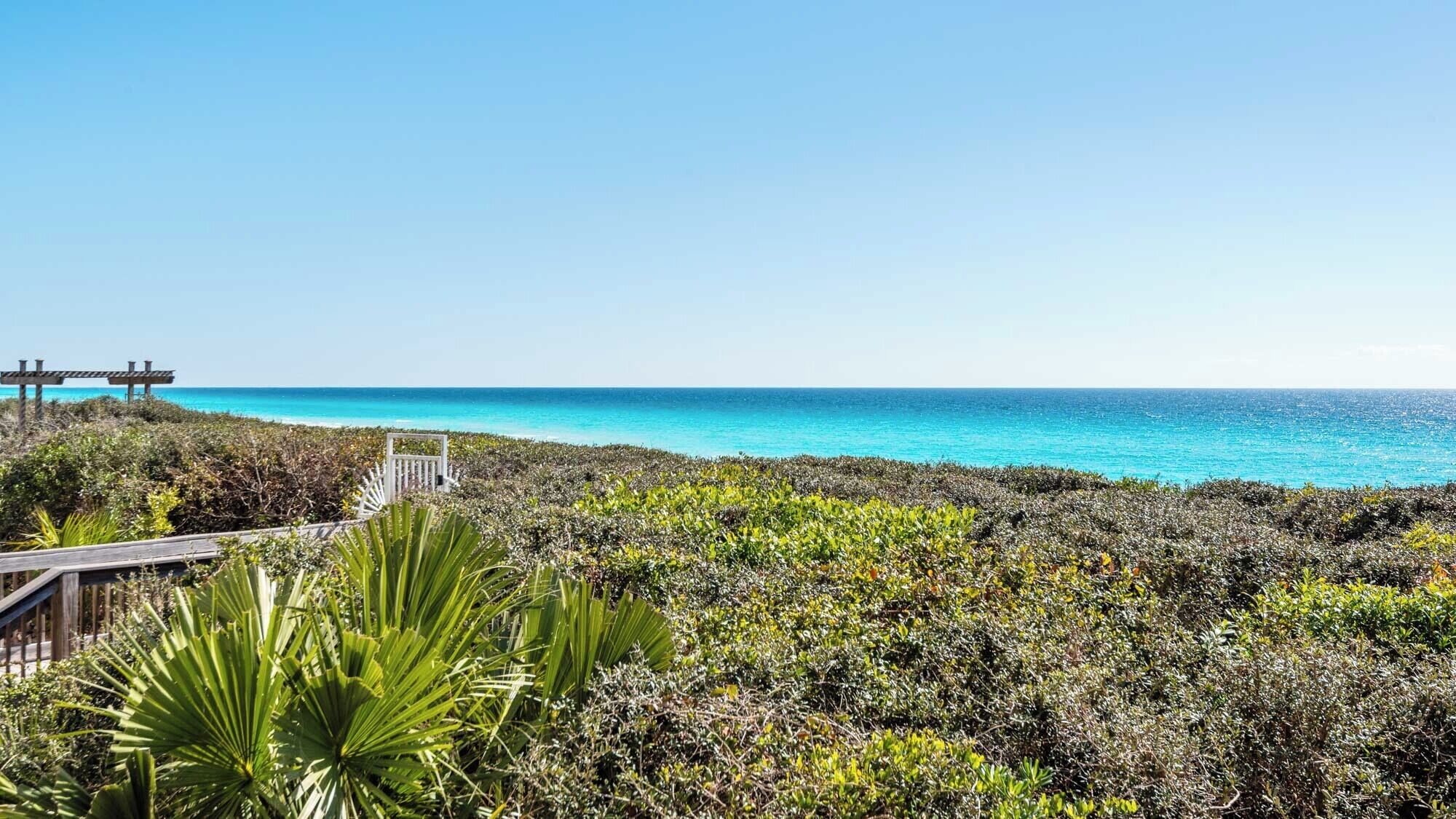 A coastal landscape with a wooden walkway leading to a gazebo overlooking the ocean.