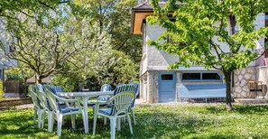 A patio with a table and chairs, a stone building with a garage door, and a tree.