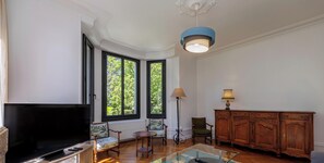 A living room with a television, two windows, a lamp, and a wooden cabinet.