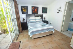 A bedroom with a bed, a nightstand, a wall-mounted lamp, and a door leading to a bathroom. - 23 Ambleside Cottage by the sea (Port Shepstone)