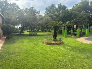 Un jardin bien entretenu, avec une pelouse, un petit arbre et un jardinier en briques orné de fleurs.