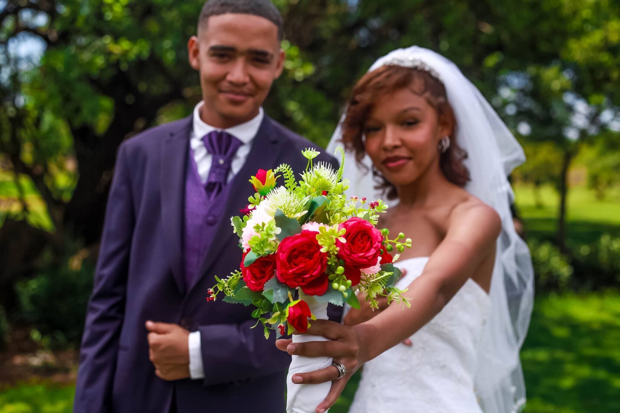 A wedding couple holding a bouquet of red roses.