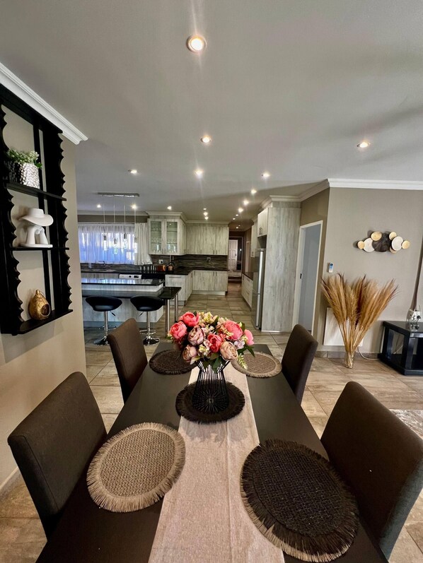 Un espace repas avec une longue table, des chaises et un vase de fleurs.