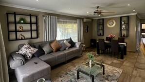 A modern living room with a grey sofa, a coffee table, and a dining area with a chandelier. - Antelope Farm Events (Akasia)