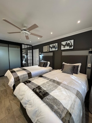 A modern hotel room with two beds, a ceiling fan, artwork on the walls, and a view of the outside.