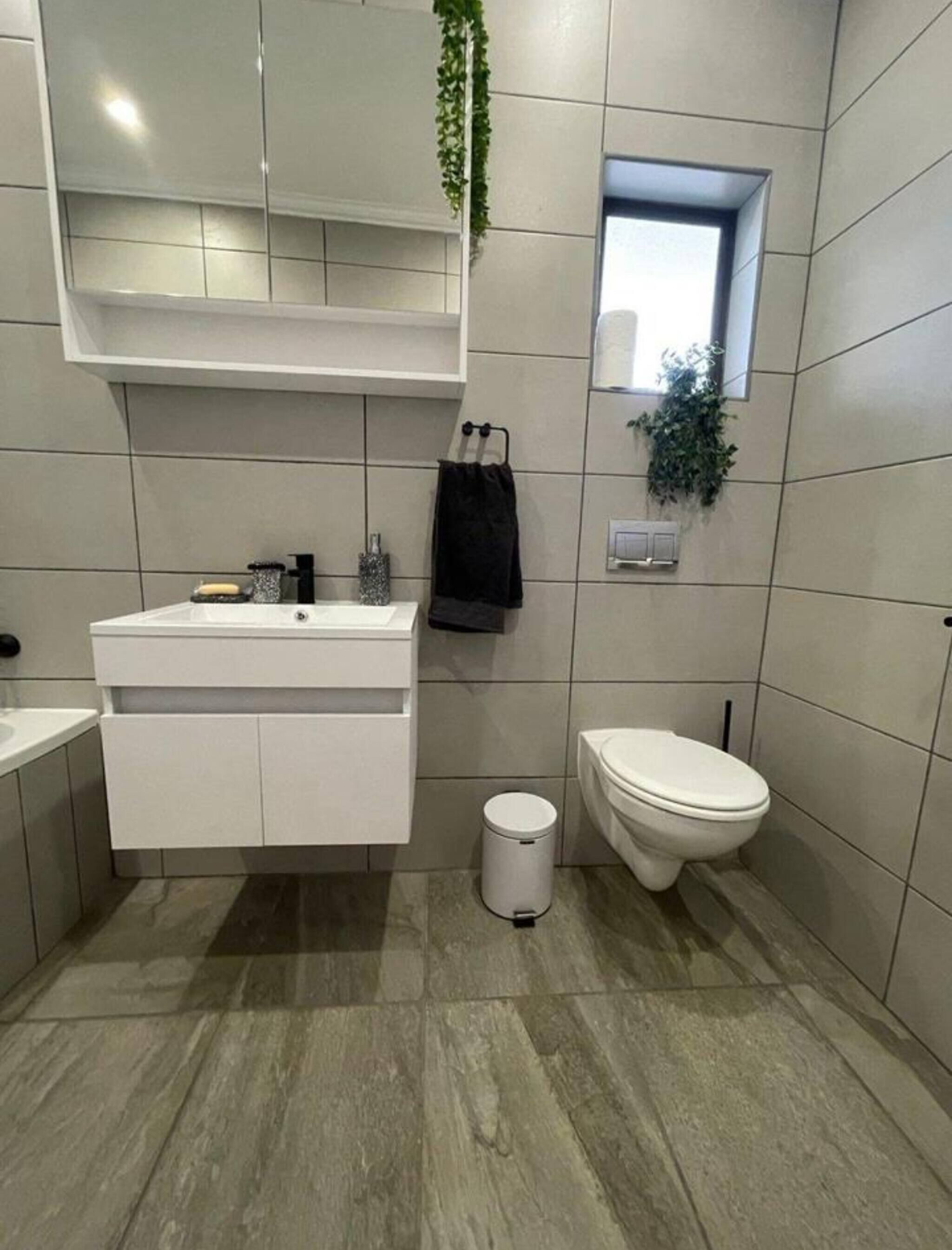 Un bagno moderno con un mobile lavabo bianco, un water e un piccolo cestino.
