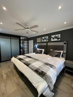 Une chambre Ă coucher moderne avec un grand lit, un ventilateur de plafond et des Ćuvres dâart accrochĂ©es aux murs.