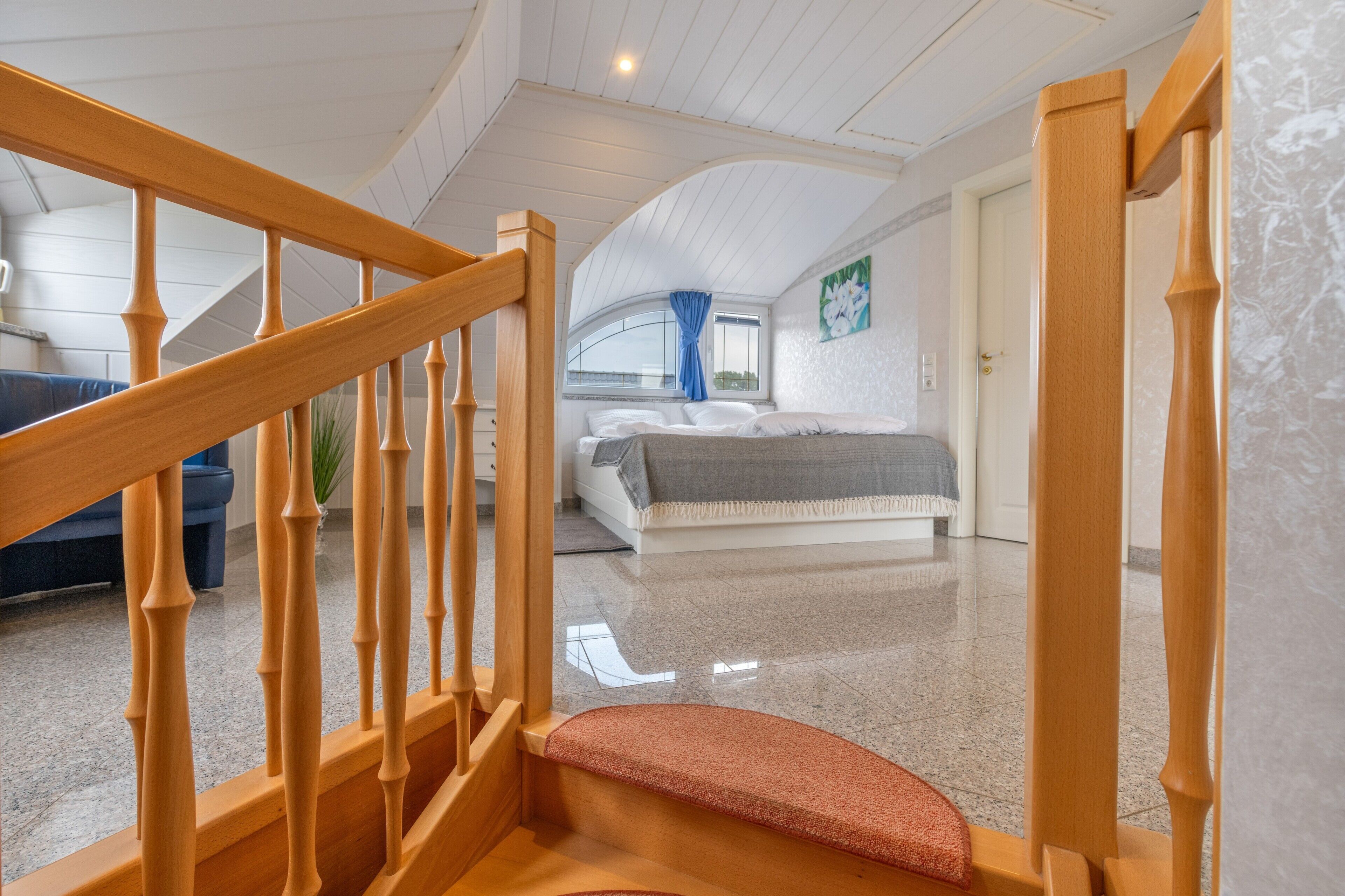 Eine Treppe führt zu einem Schlafzimmer mit einem Bett, einem Fenster mit Vorhängen und einer Tür.