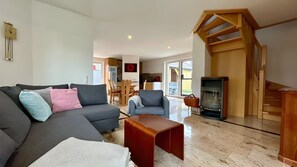 Een woonkamer met een bank, fauteuil, salontafel, open haard en een trap.