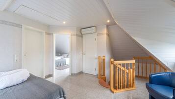 Una camera da letto con un letto, una sedia di legno, un divano blu e una scala che conduce a un piano superiore.