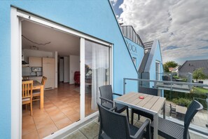 A modern outdoor dining area with a table and chairs, a sliding glass door leading to a kitchen, and a blue exterior wall with the text 'OCA'. - Lakefront Residence for 18 Guests (320 m²) in Untergöhren (Göhren-Lebbin)