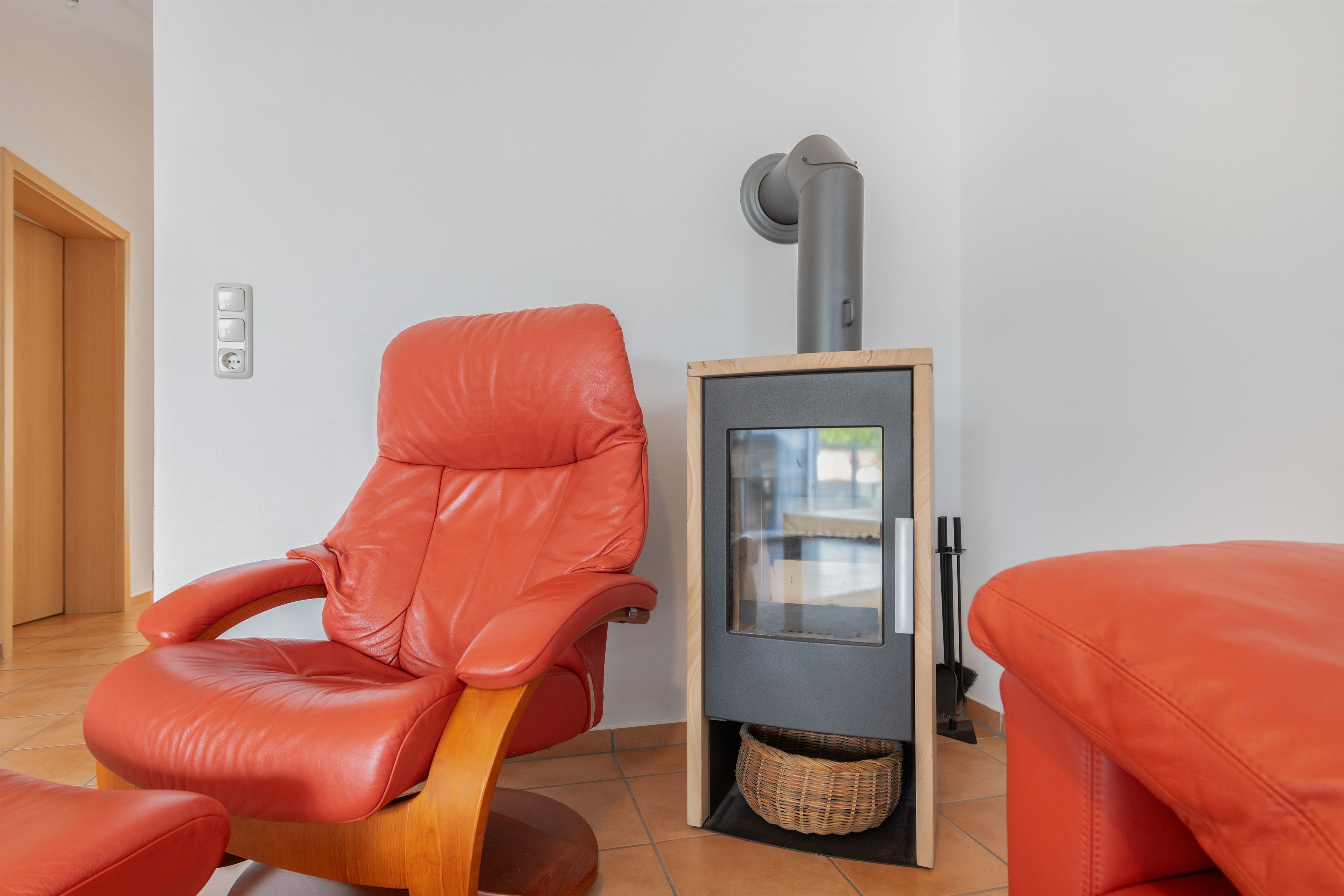A room with a red leather chair, a small heater, and a wicker basket.