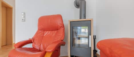 Una habitación con una butaca de cuero rojo, un calentador pequeño y una cesta de mimbre.
