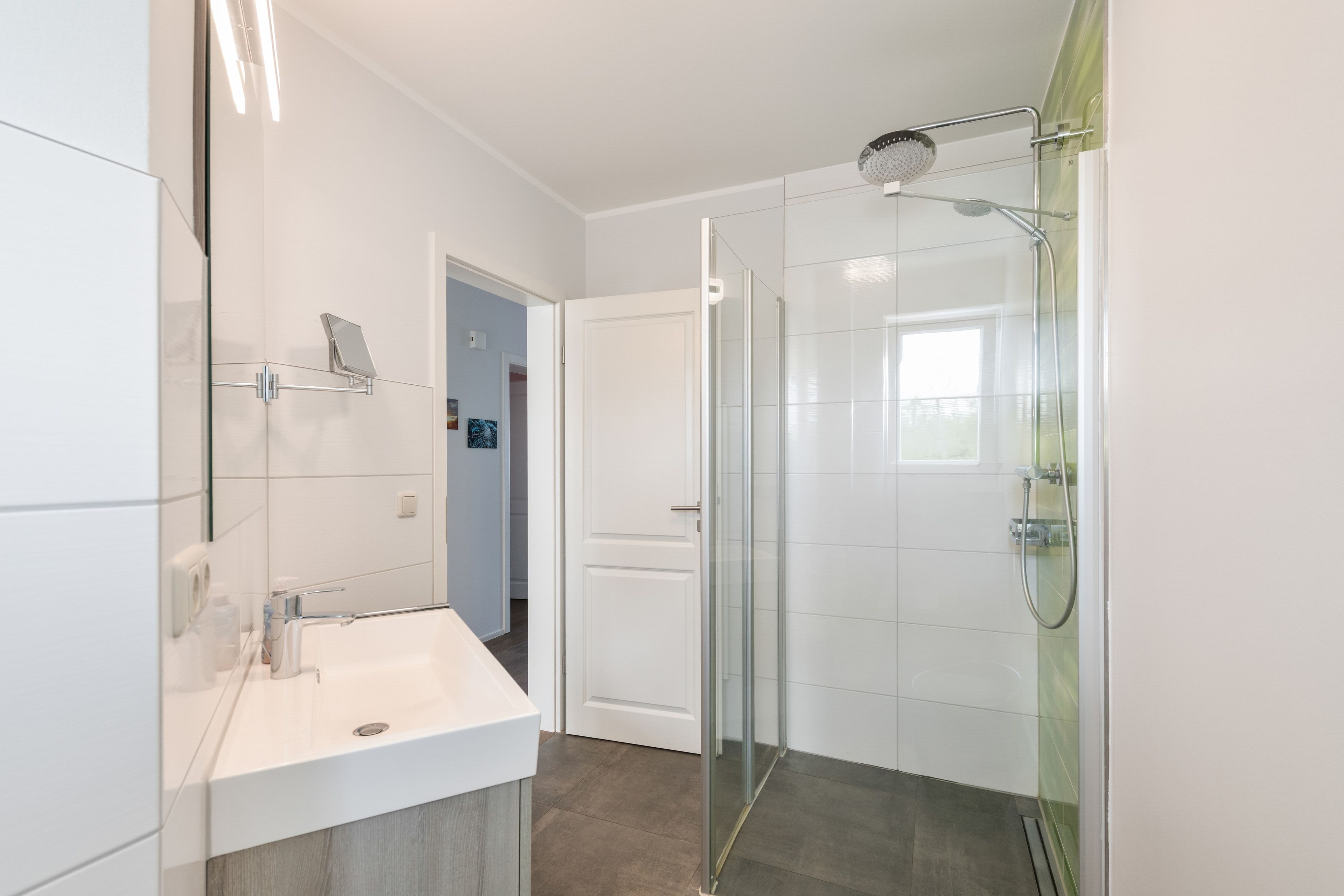 A modern bathroom with a glass shower enclosure, a white sink, and a door leading to another room.