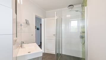 A modern bathroom with a glass shower enclosure, a white sink, and a door leading to another room.