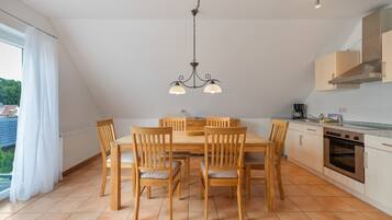 Un comedor con mesa y sillas de madera, una araña y una cocina con electrodomésticos modernos.