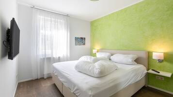 Een hotelkamer met een bed, een aan de muur bevestigde televisie, een raam met dunne gordijnen en een groene accentmuur.