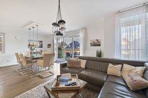 A modern living room with a sofa, a dining table, and a kitchen in the background. - Lakefront Residence for 18 Guests (320 m²) in Untergöhren (Göhren-Lebbin)